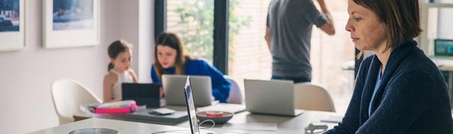 woman reviewing finances on laptop, family in background