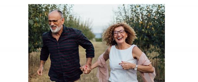 husband and wife running through field, holding hands