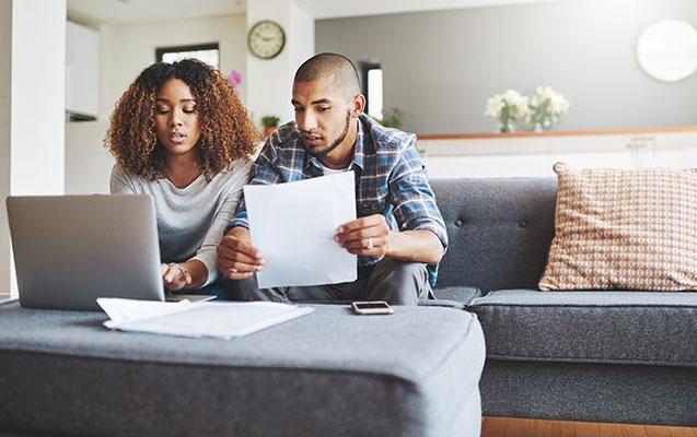 a couple sits in living room reviewing financial documents