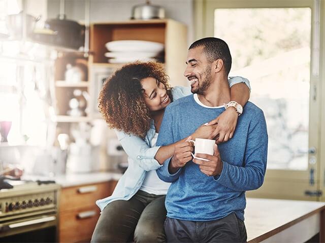 a husband and wife sit together in kitchen smiling and laughing